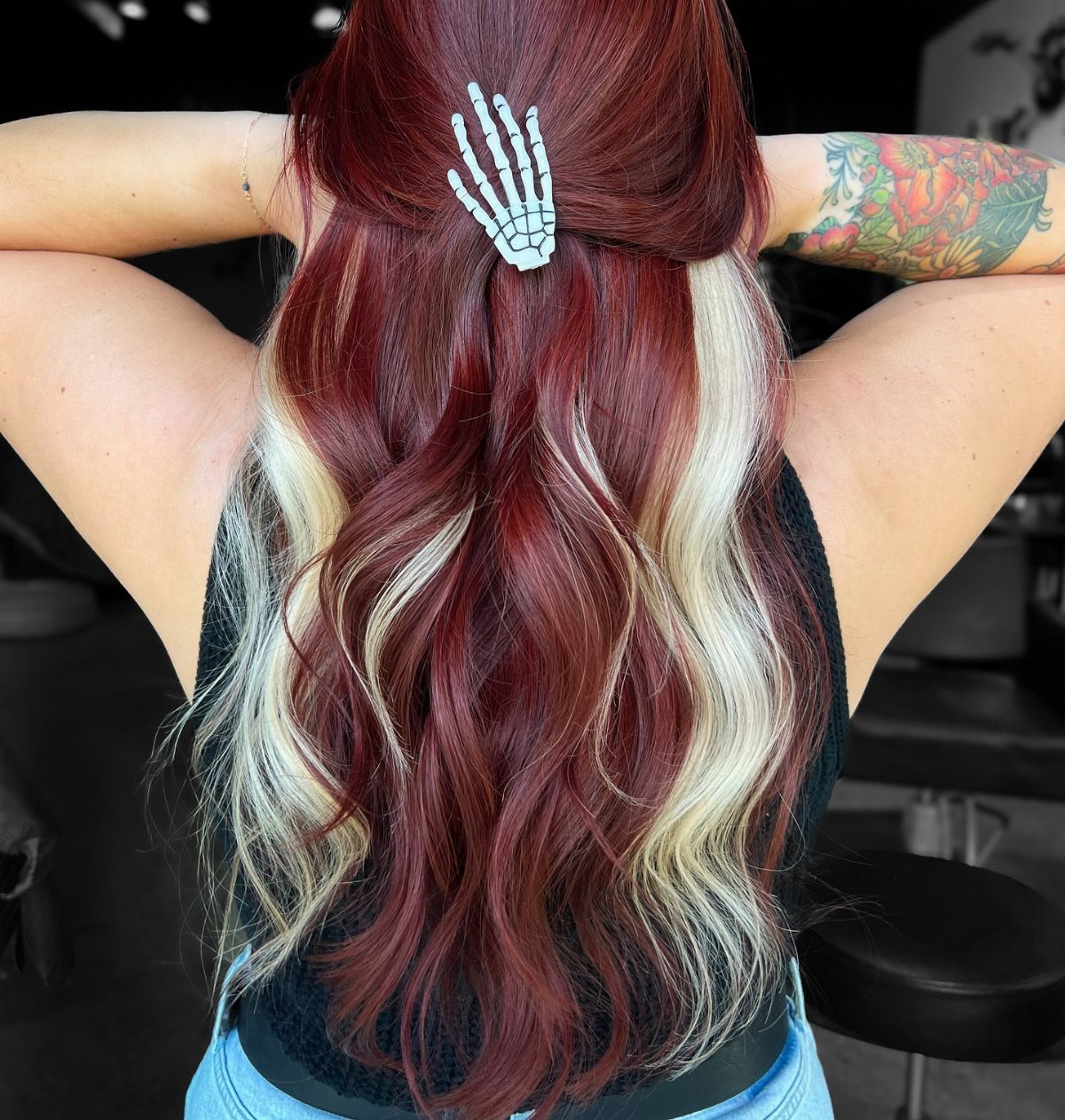 Long burgundy-red waves with broad blonde streaks and a skeleton-hand clip