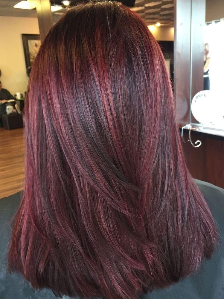 Long cherry-red hair with burgundy highlights and layered ends in a salon