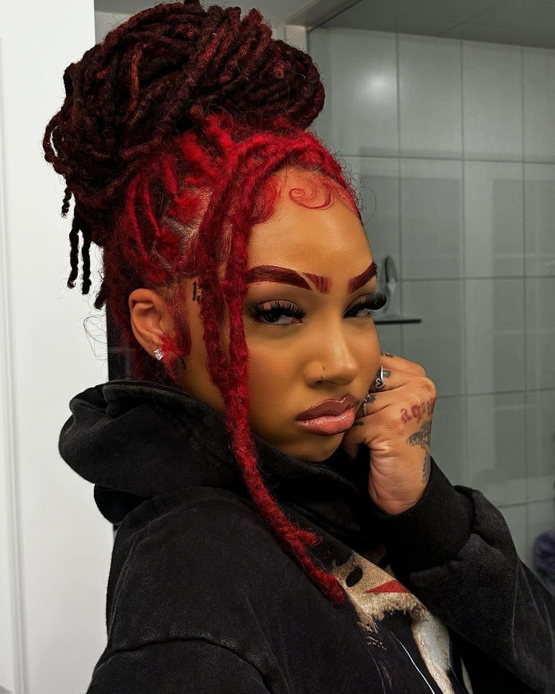 Woman with dark-rooted cherry-red locs gathered in a high bun