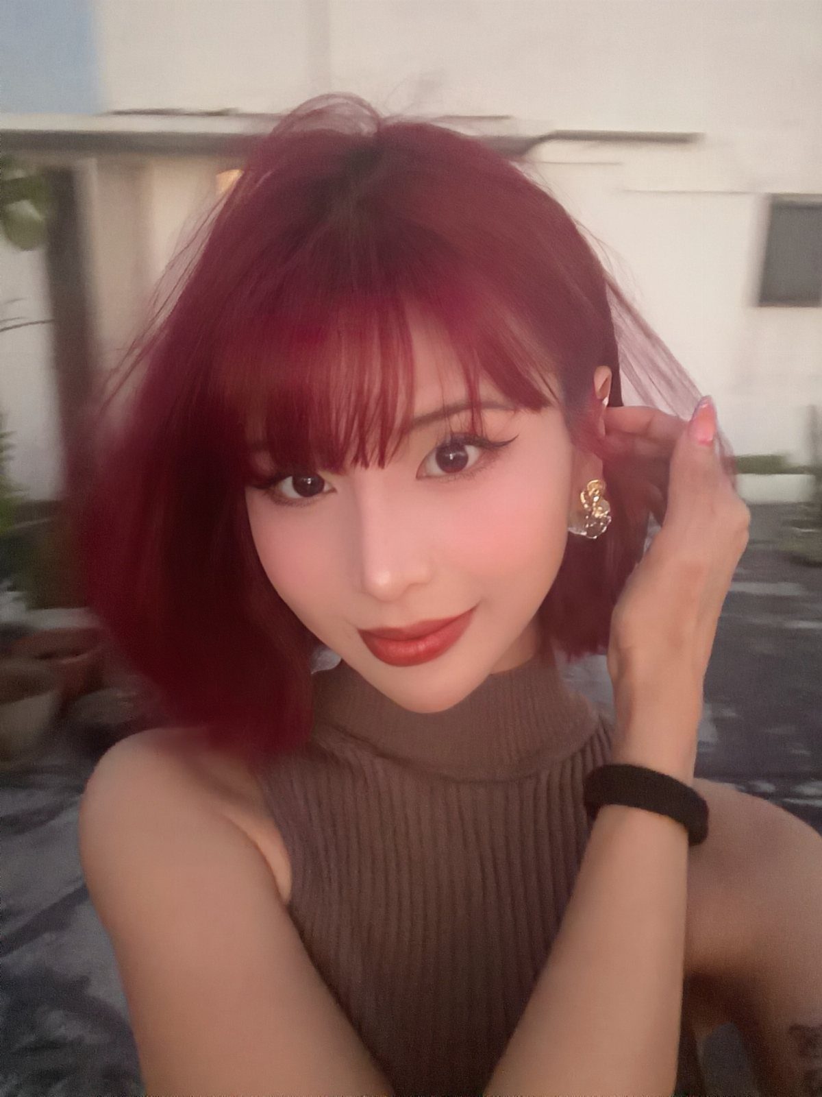 Woman with deep cherry-red hair and blunt bangs poses indoors