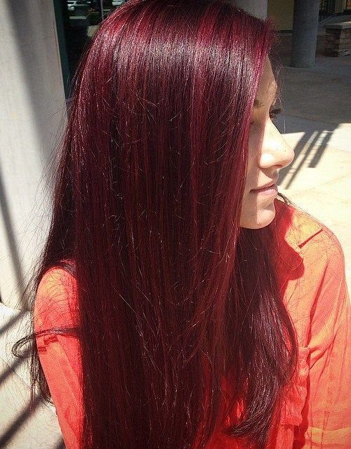 Long, straight cherry-red hair shines in sunlight over an orange top.