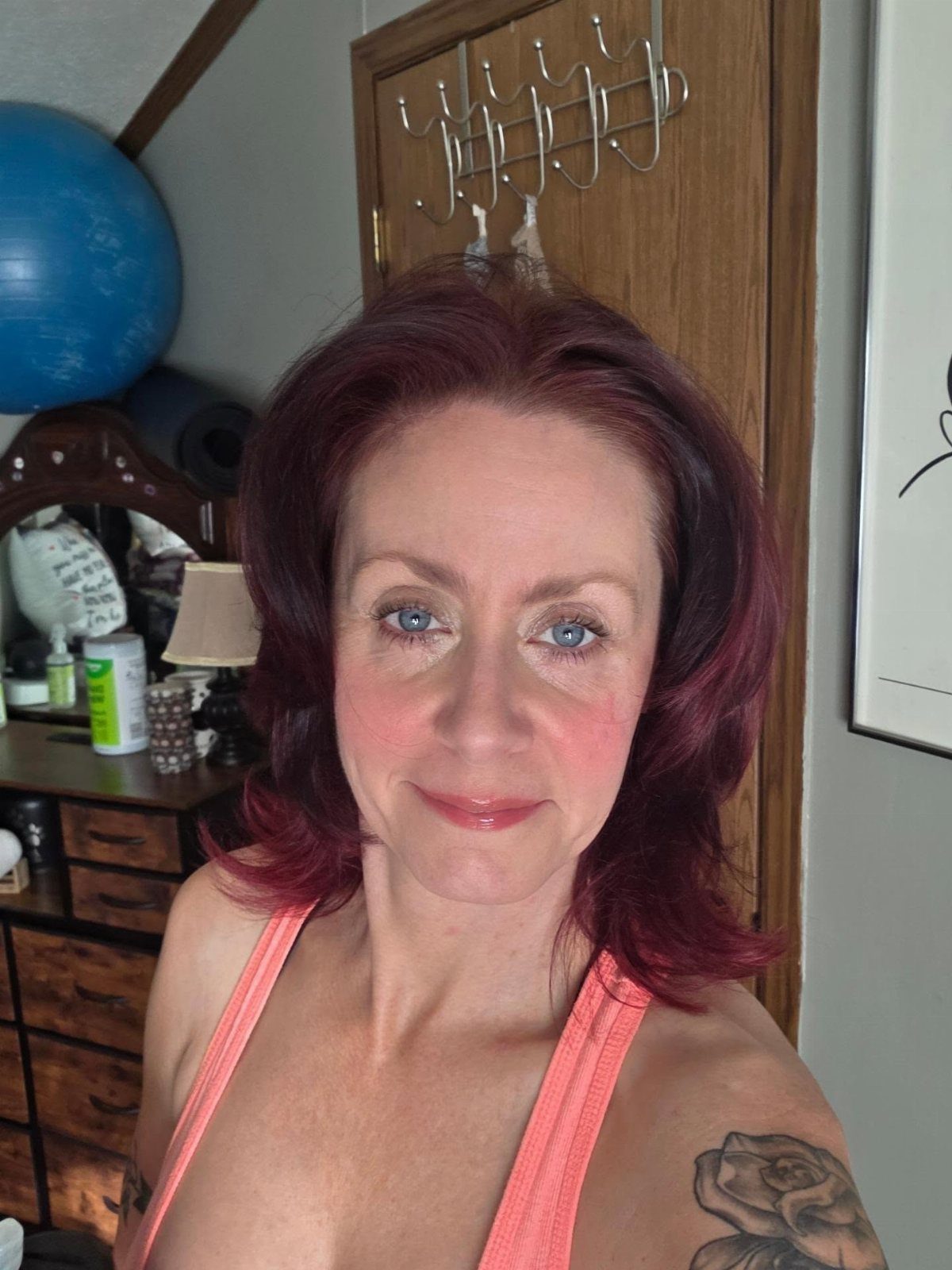 Woman with shoulder-length dark cherry-red hair posing indoors in a coral tank top