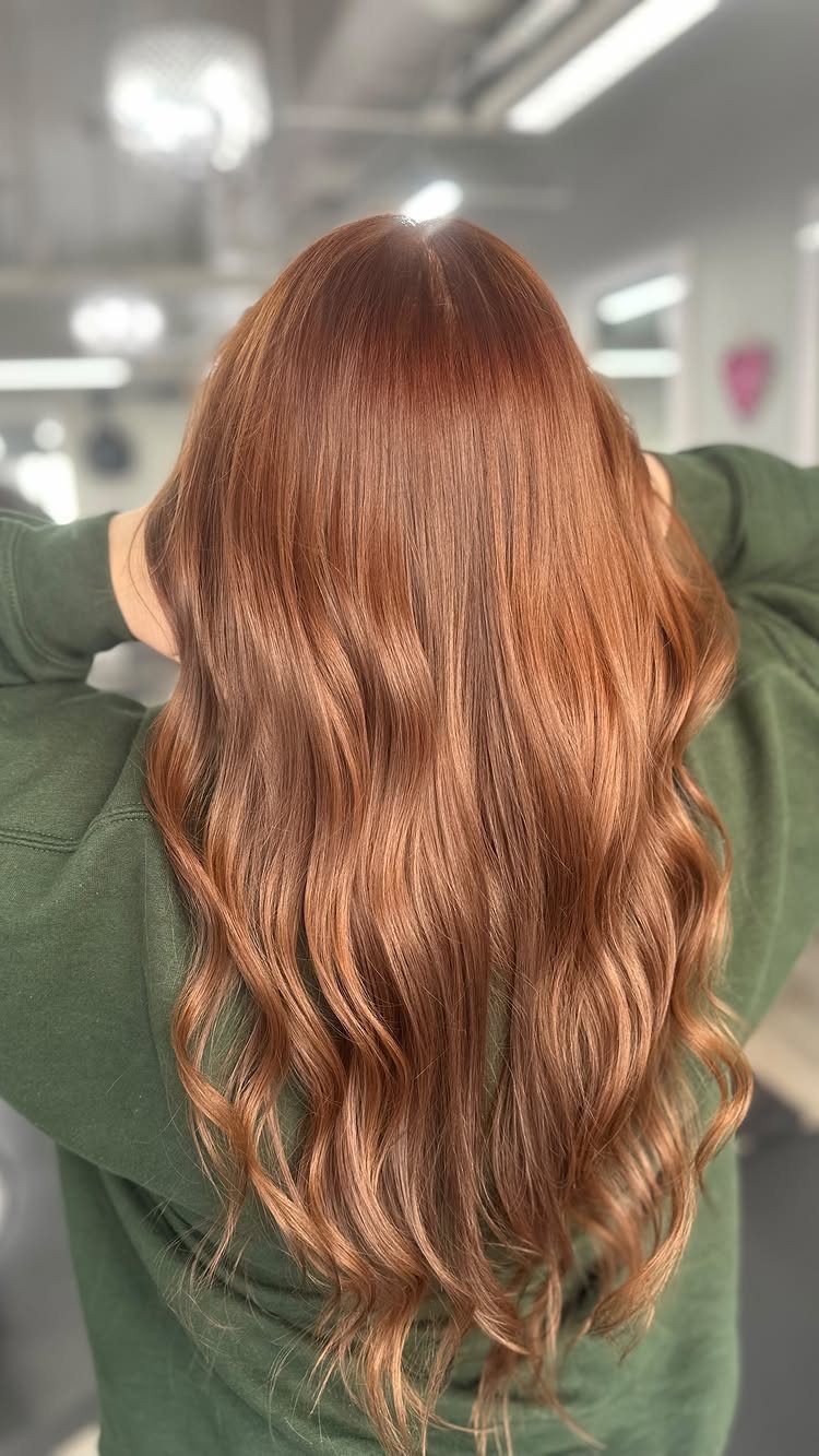 Long wavy coppery reddish-brown hair falls over a green top