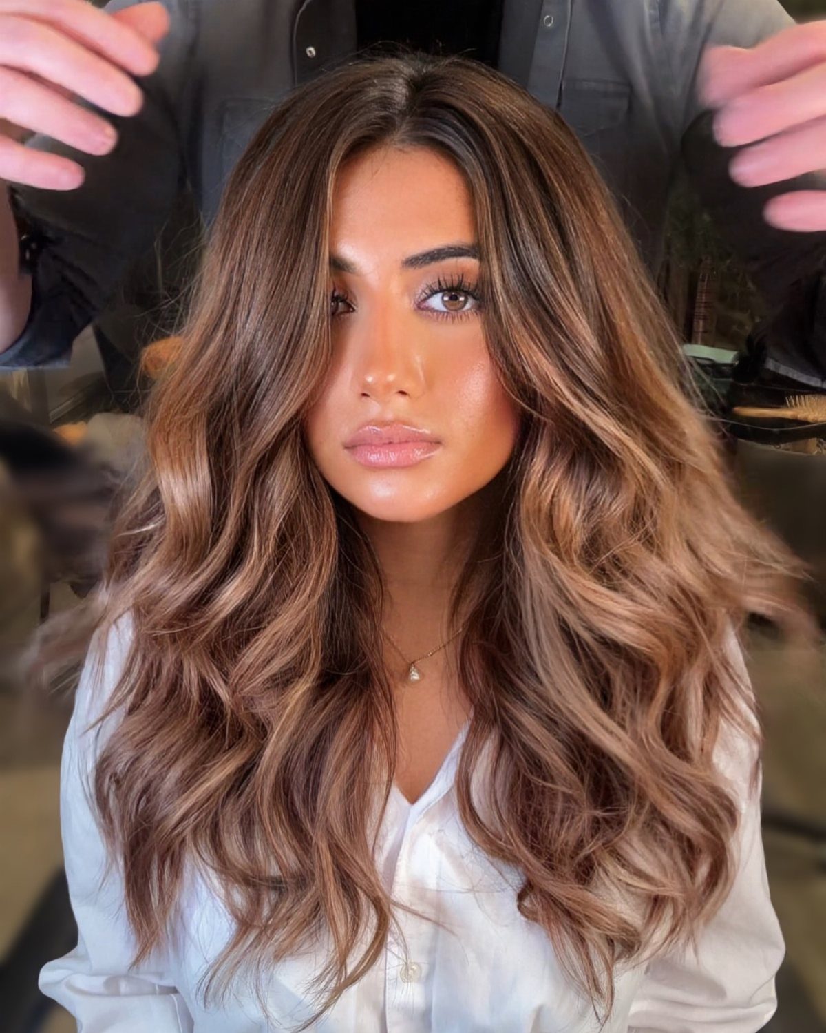Woman displaying long chestnut-brown waves with contrasting caramel highlights in a salon