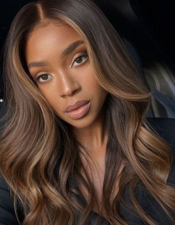 Woman with long chestnut brown waves and subtle highlights posing against a dark background