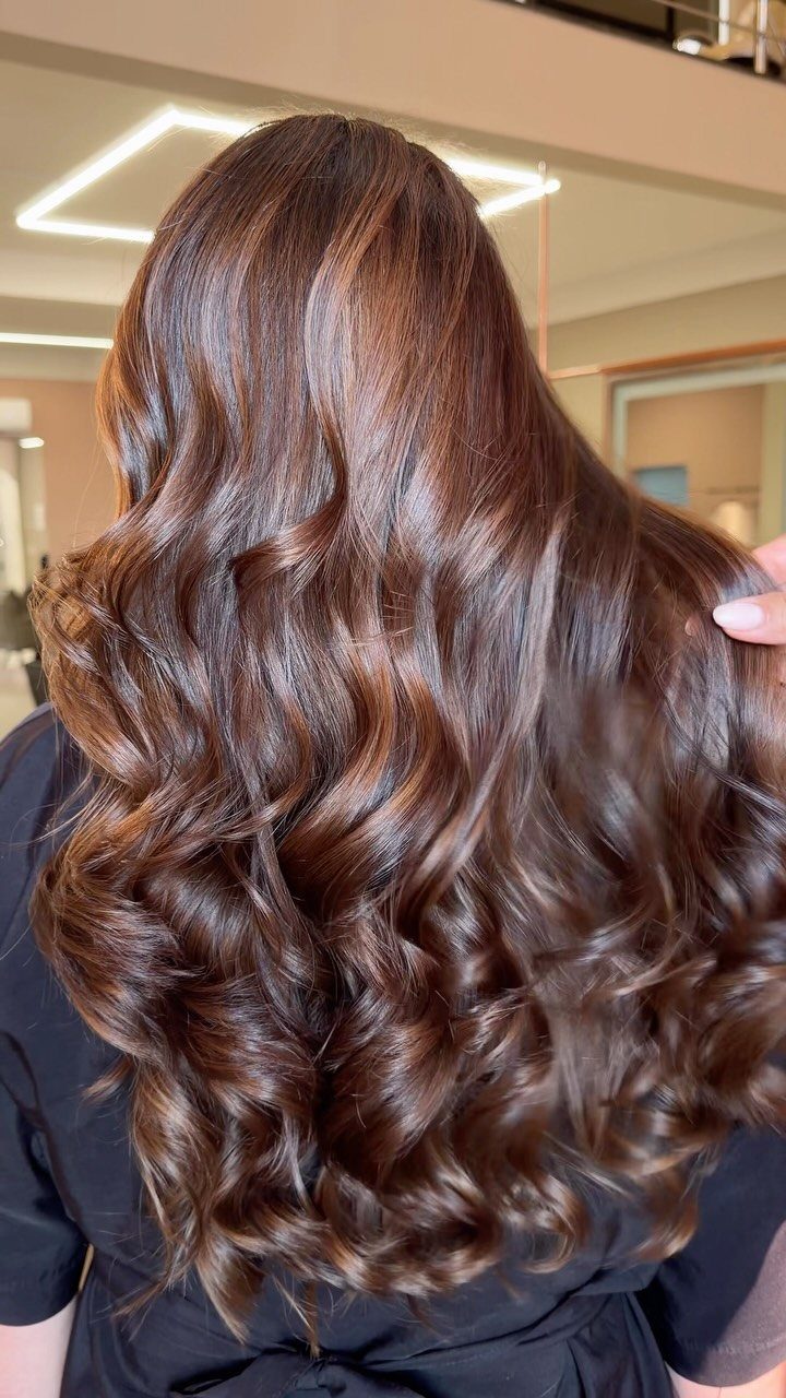 Long chocolate chestnut brown hair falls in glossy, defined waves
