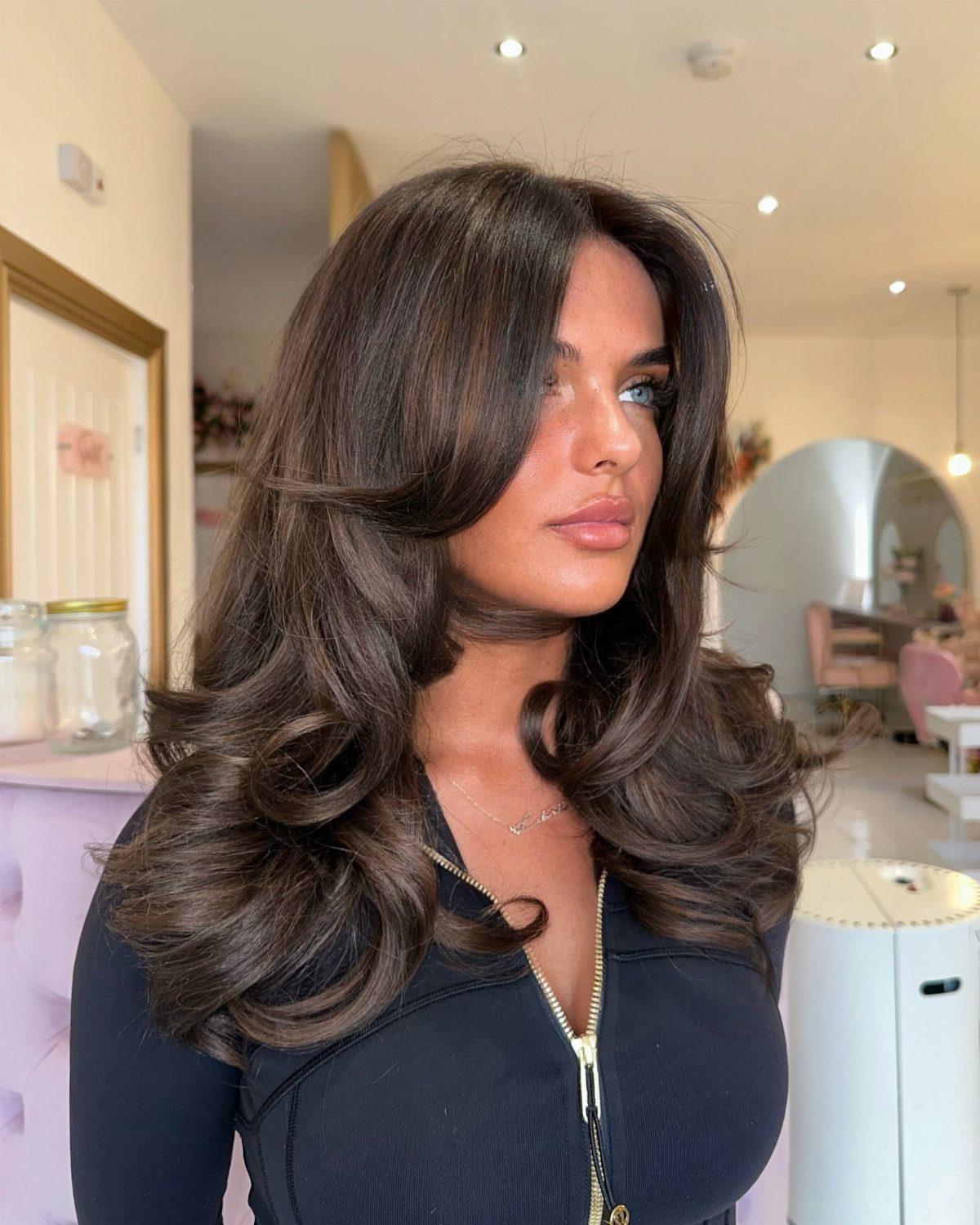 Long dark chestnut brown hair falls in glossy, loose layered waves around a woman’s shoulders