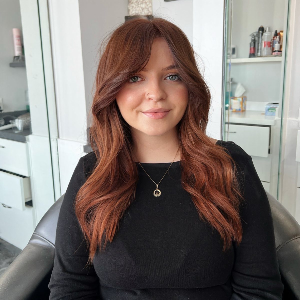 Woman with long, wavy reddish chestnut-brown hair seated in a salon chair