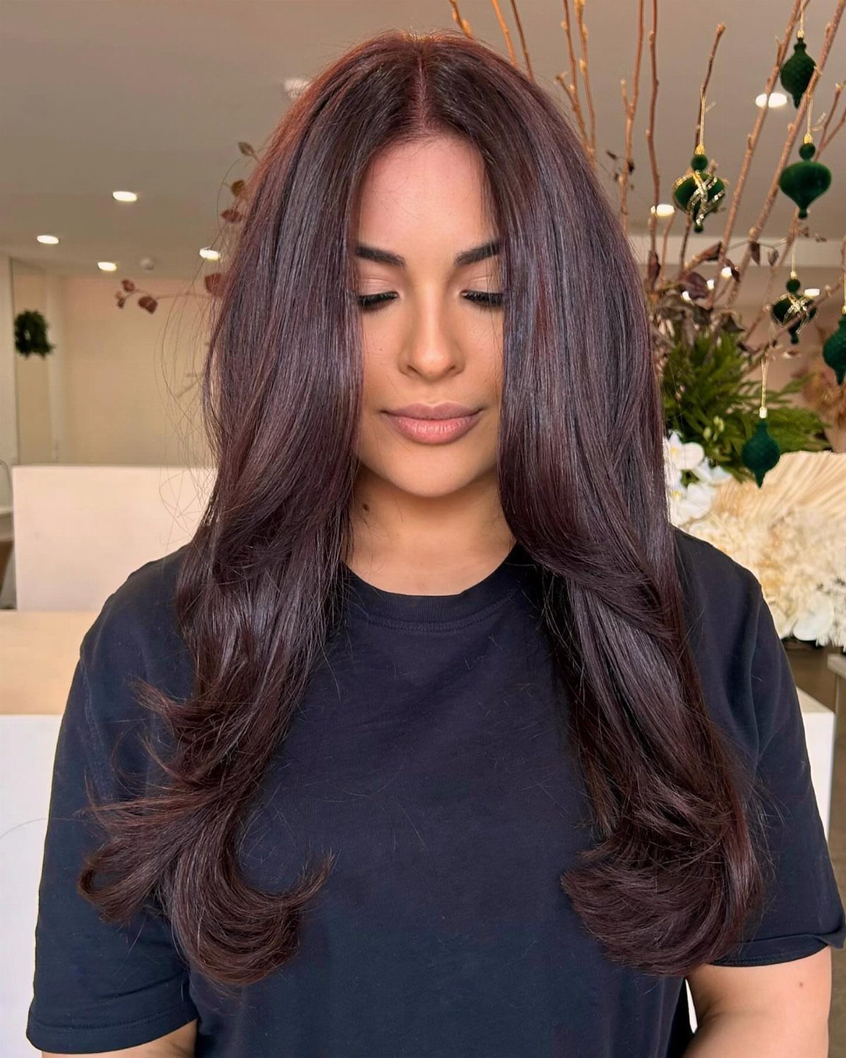 Woman displays glossy, dark eggplant-brown hair with long curled ends in a salon.