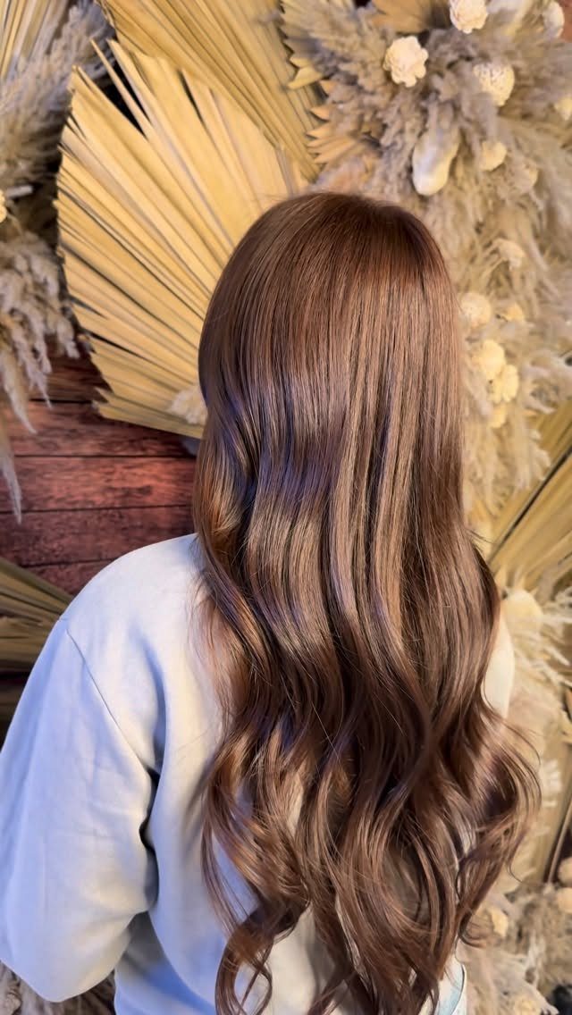 Long glossy chestnut-brown waves drape over a pale blue top