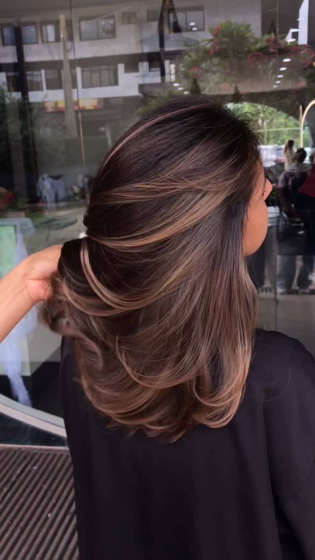 Layered chestnut hair with lighter balayage streaks, lifted by a hand