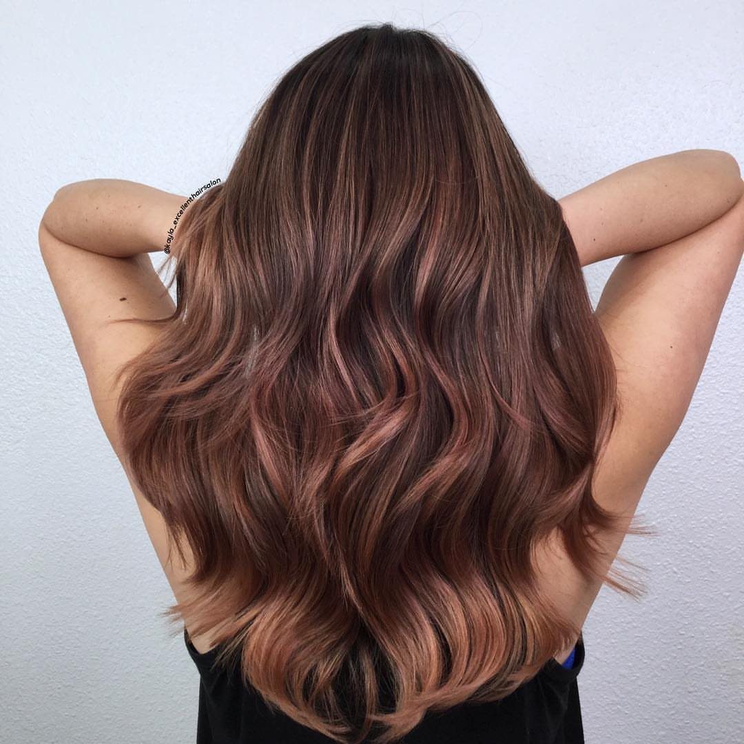 Wavy chestnut hair with rose-gold tones cascading down a person's back