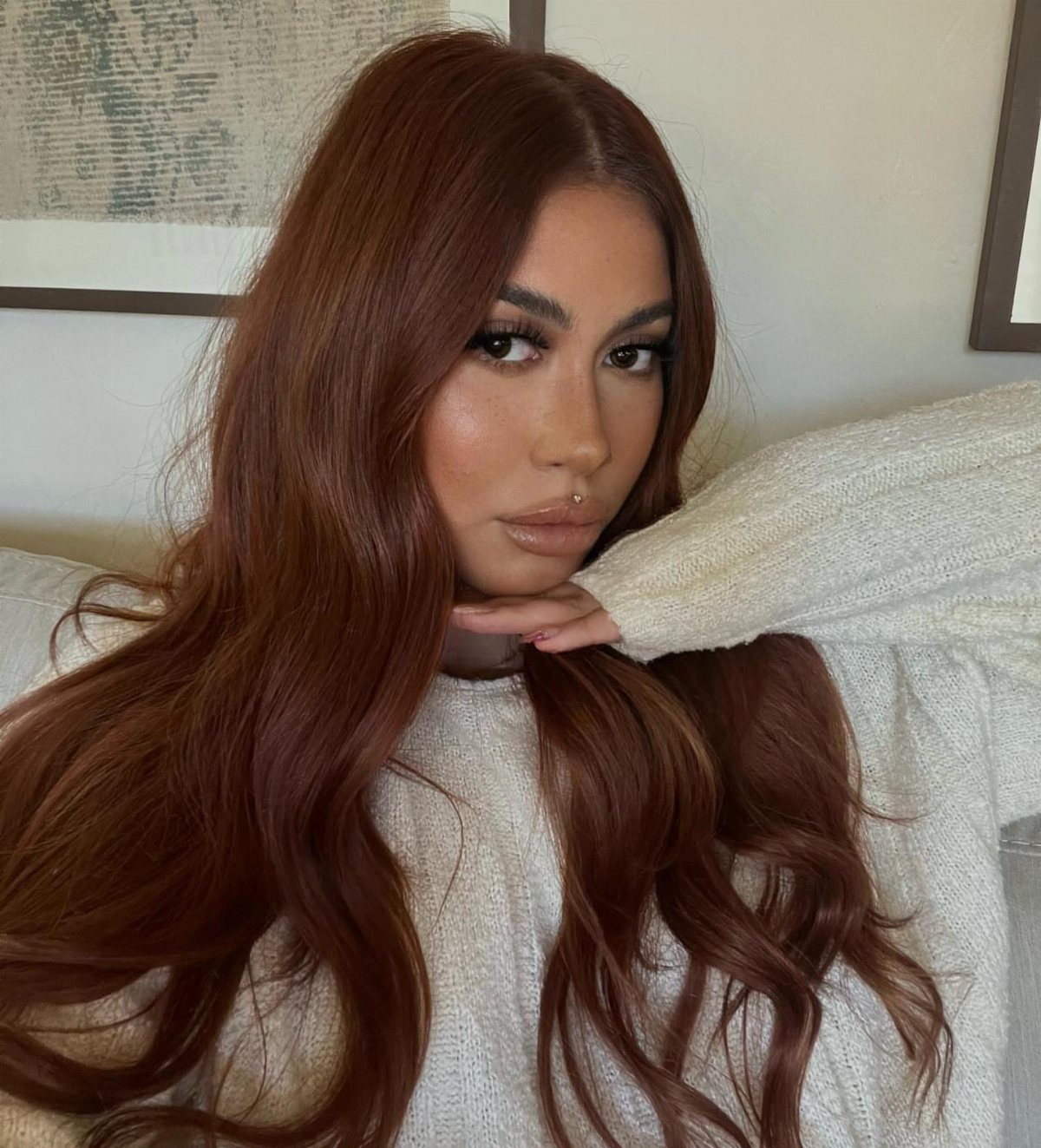 Woman with long, glossy reddish-brown waves wearing a cream sweater