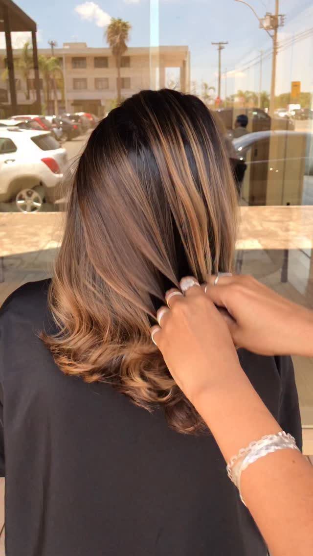 Brunette hair with honey highlights curled at the ends as a hand holds a section