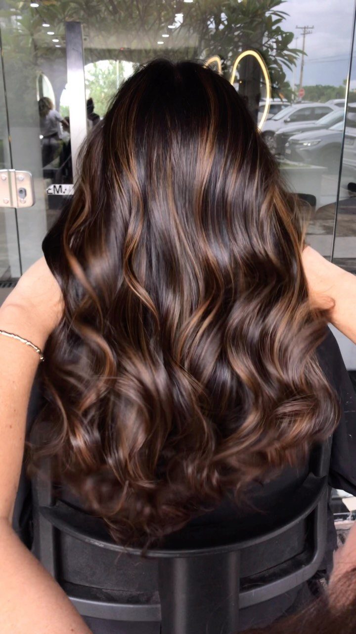 Long wavy chestnut hair with warm red balayage highlights shown from behind