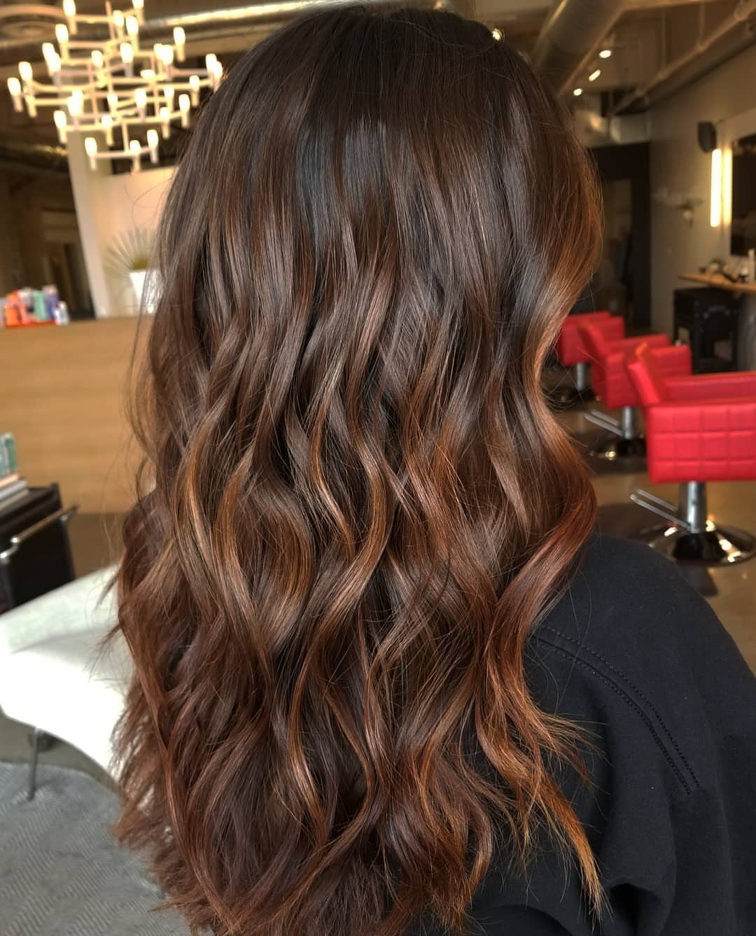 Long brunette waves show warm caramel balayage highlights in a salon