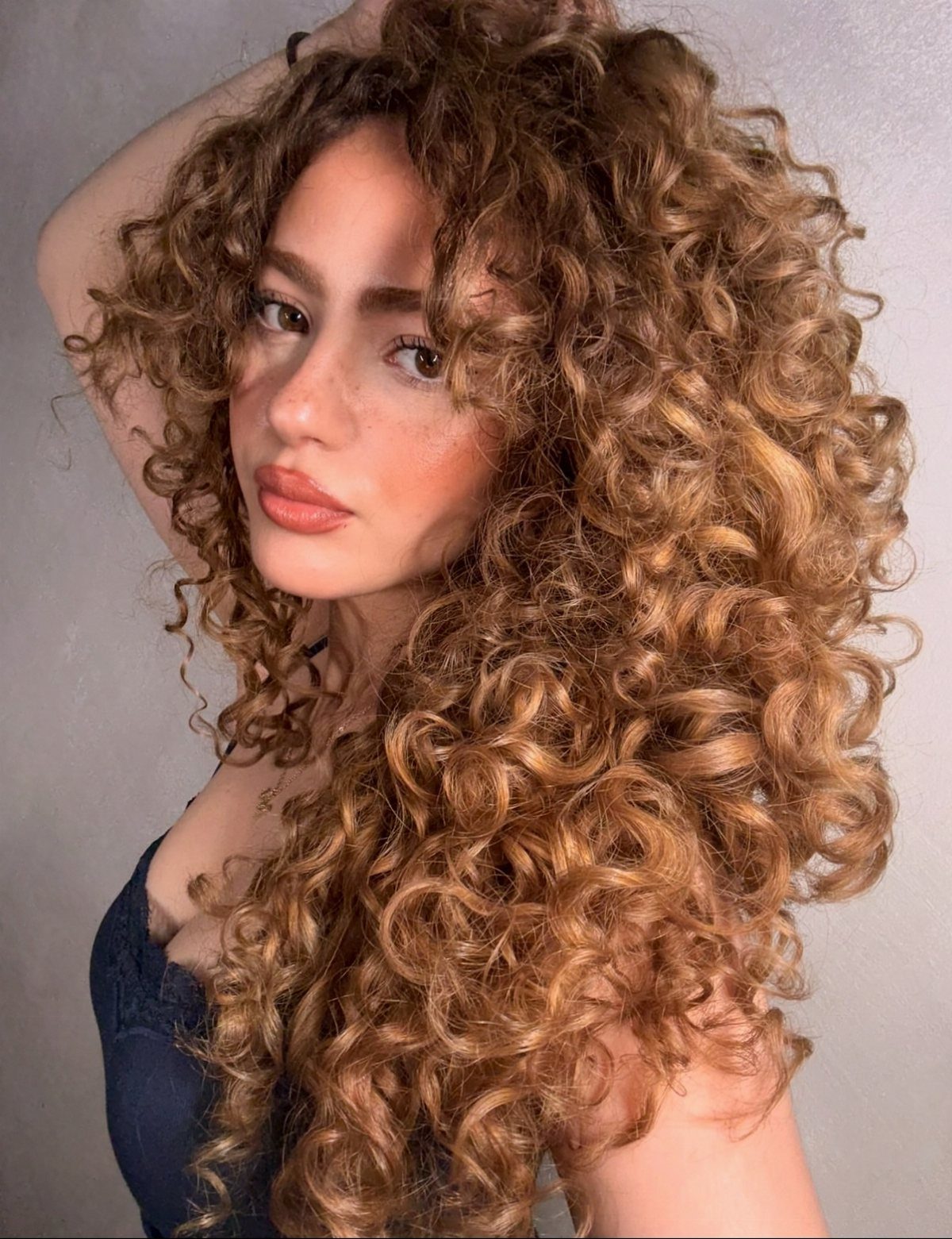 Woman with long, defined chestnut curls and warm copper balayage highlights
