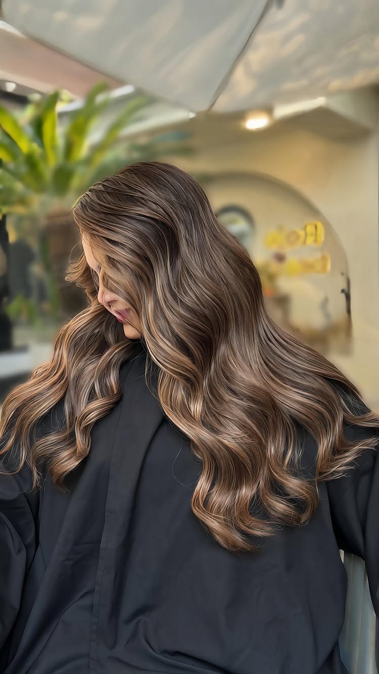 Long wavy brunette hair with dark roots and chestnut highlights in a salon