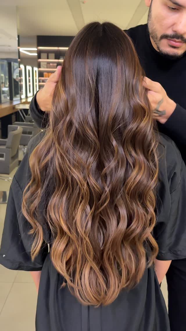 Long chestnut waves blend dark roots with warm caramel highlights