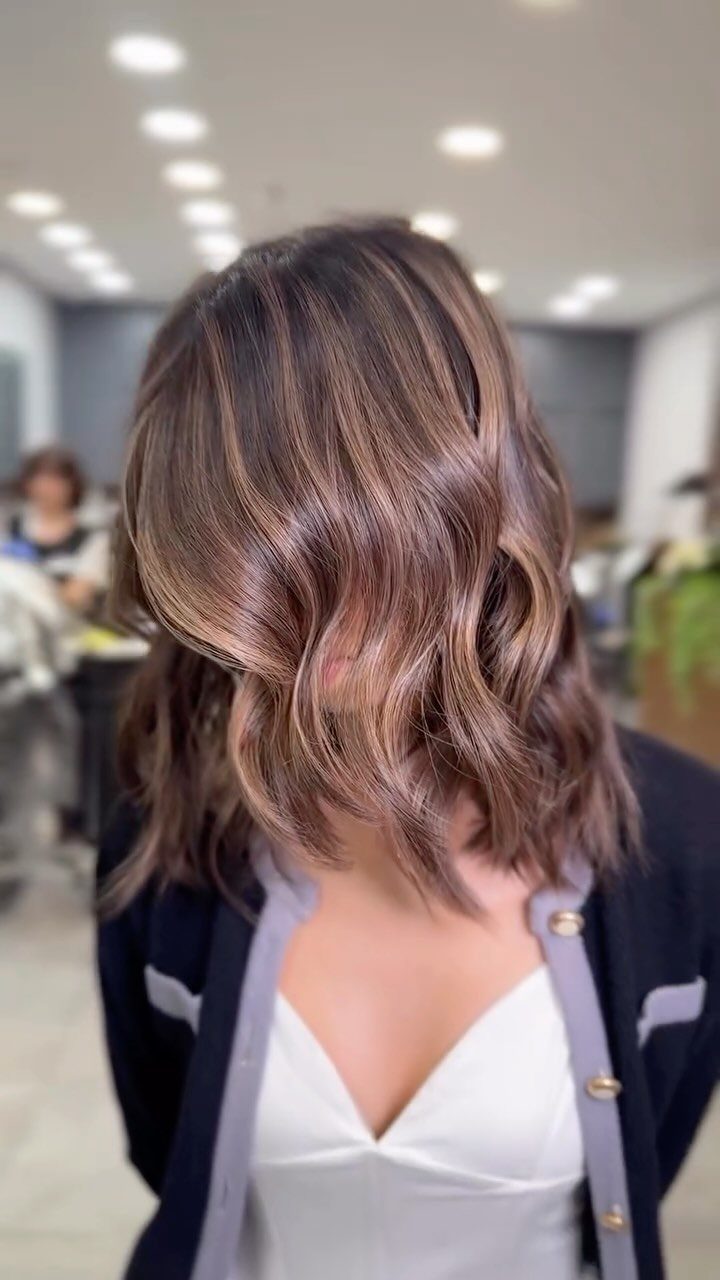Woman showing wavy chocolate hair with dimensional caramel ribbons in a salon