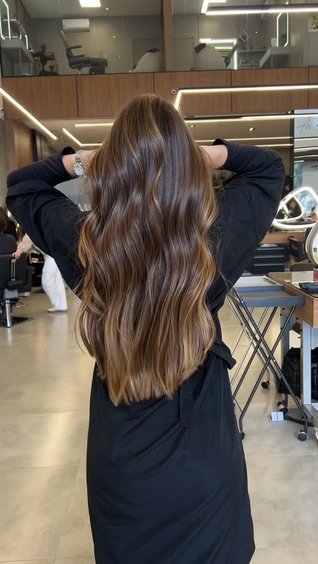 Long wavy brown hair with lighter highlights shown from behind in a salon
