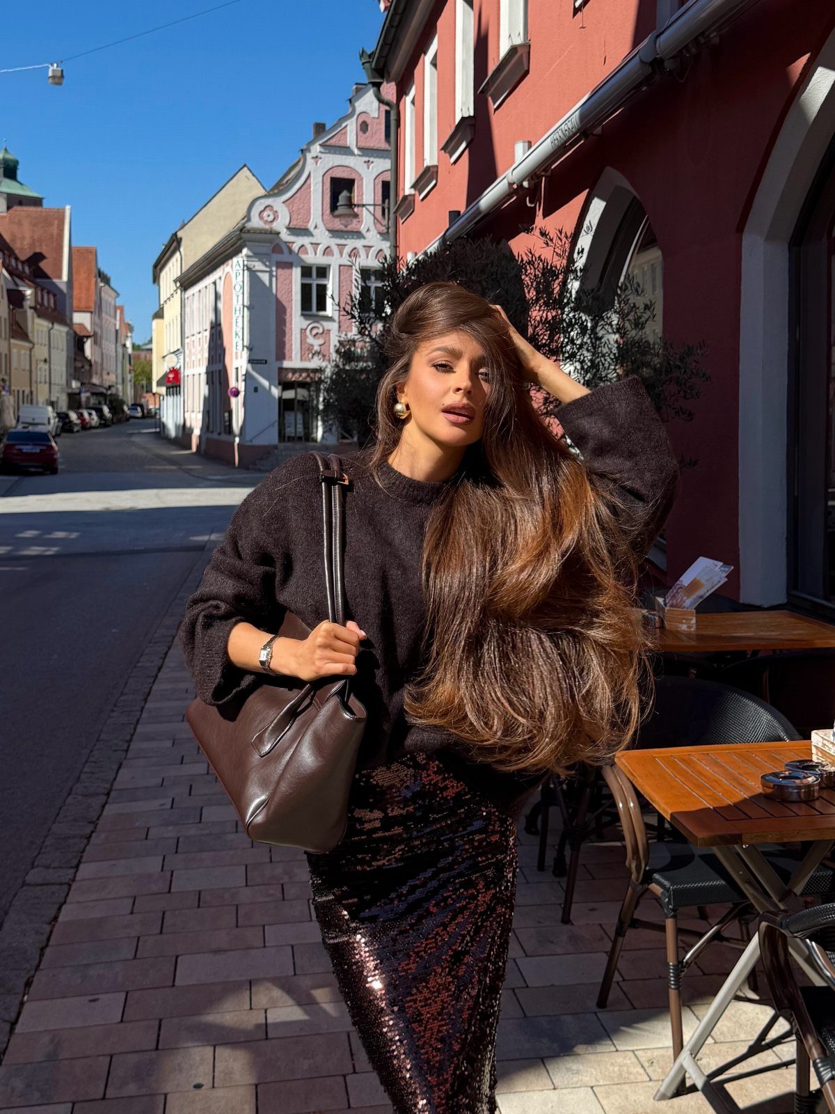 Woman with long brown hair and honey-toned strands posing on a sunny street