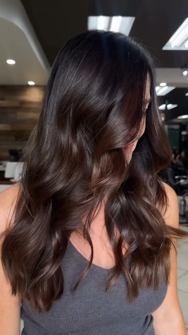 Long, glossy dark brunette hair styled in loose waves in a salon