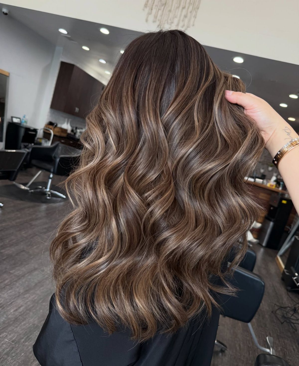 Wavy brunette hair with warm butterscotch balayage ribbons in a salon