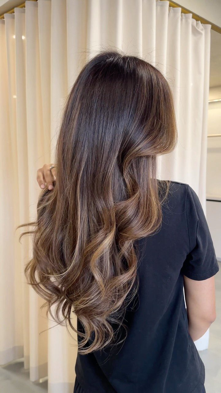 Long wavy brunette hair with blended caramel highlights against cream curtains