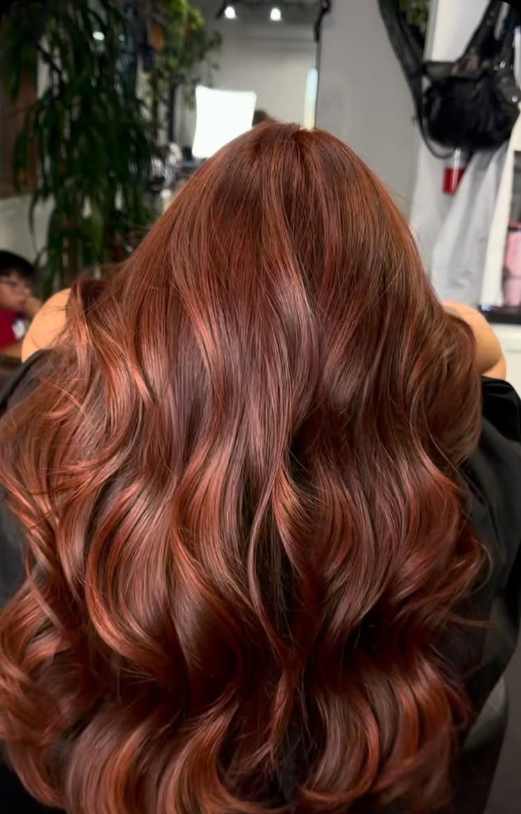 Long, glossy chocolate-brown hair with warm cherry-red tones in loose waves