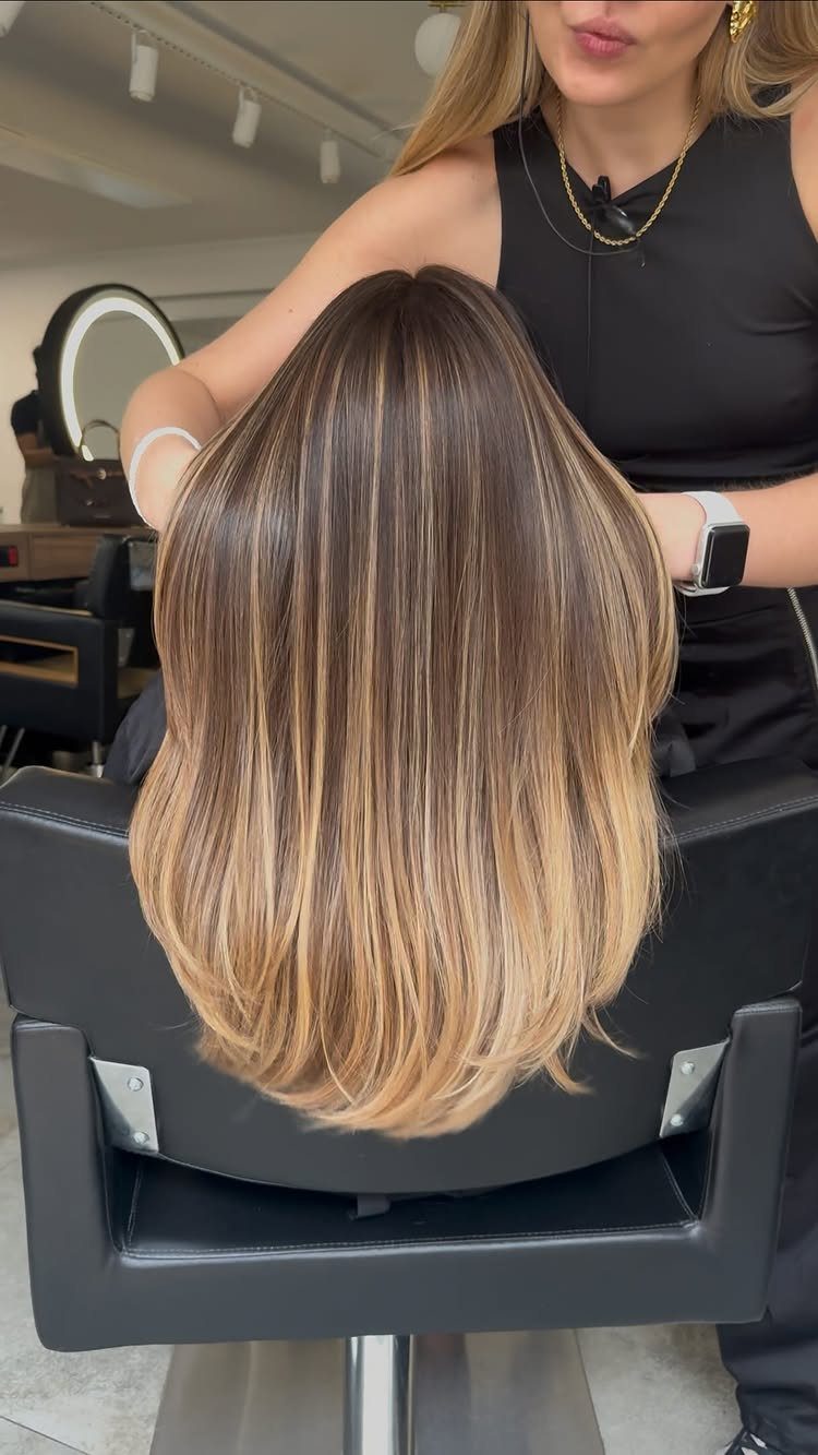 Long brown hair with warm blonde highlights in a salon chair