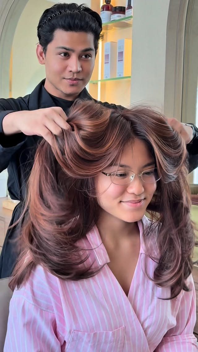 Long layered brown hair with warm rose-gold highlights styled by a hairstylist