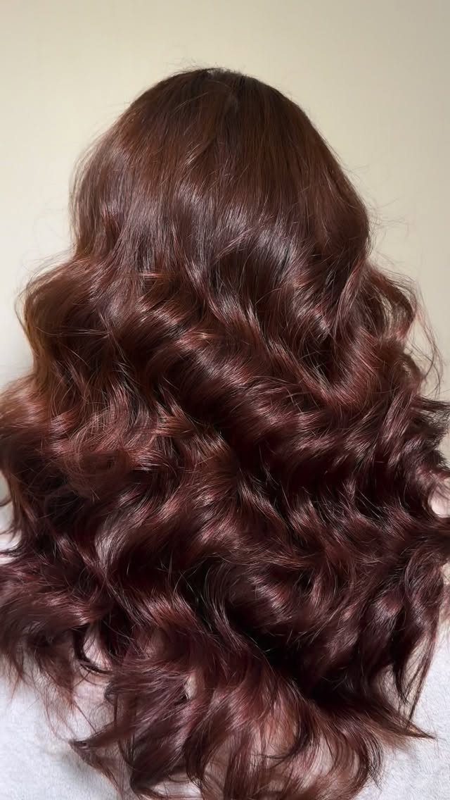 Long wavy chestnut-brown hair with subtle copper tones against a light wall