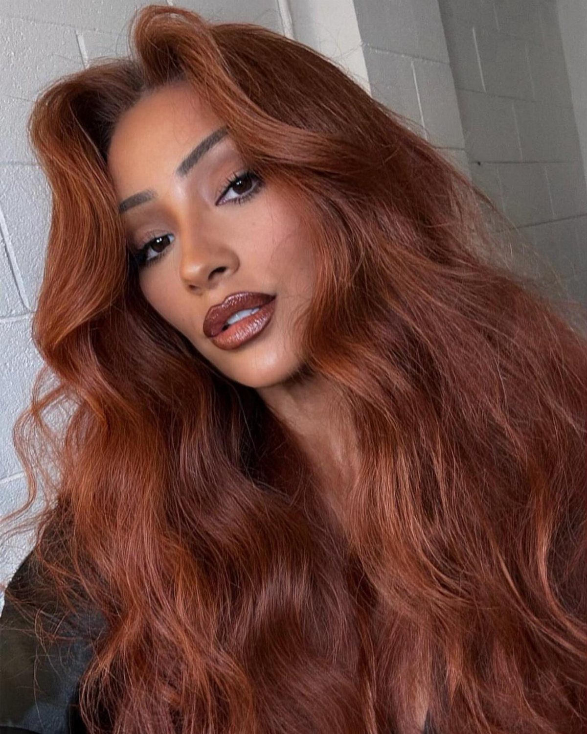 Woman posing with long, wavy copper auburn hair against a tiled wall