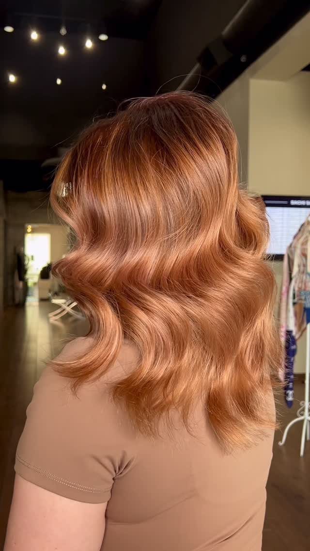 Wavy copper blonde hair with lighter streaks styled at shoulder length in a salon
