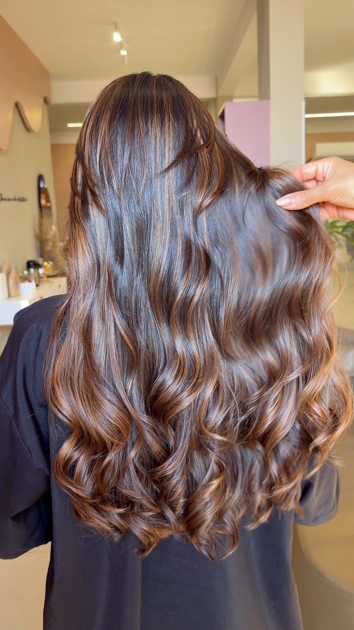 Long wavy chocolate brown hair with subtle copper highlights in a salon