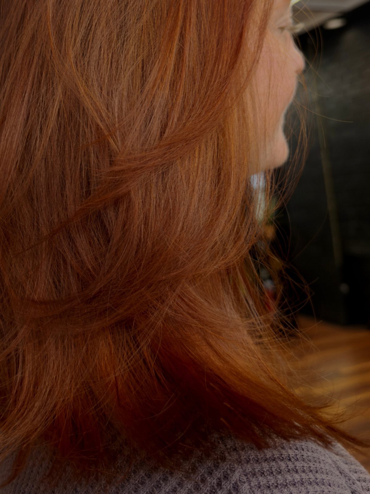 Long copper hair falls in soft layers over a gray knit top