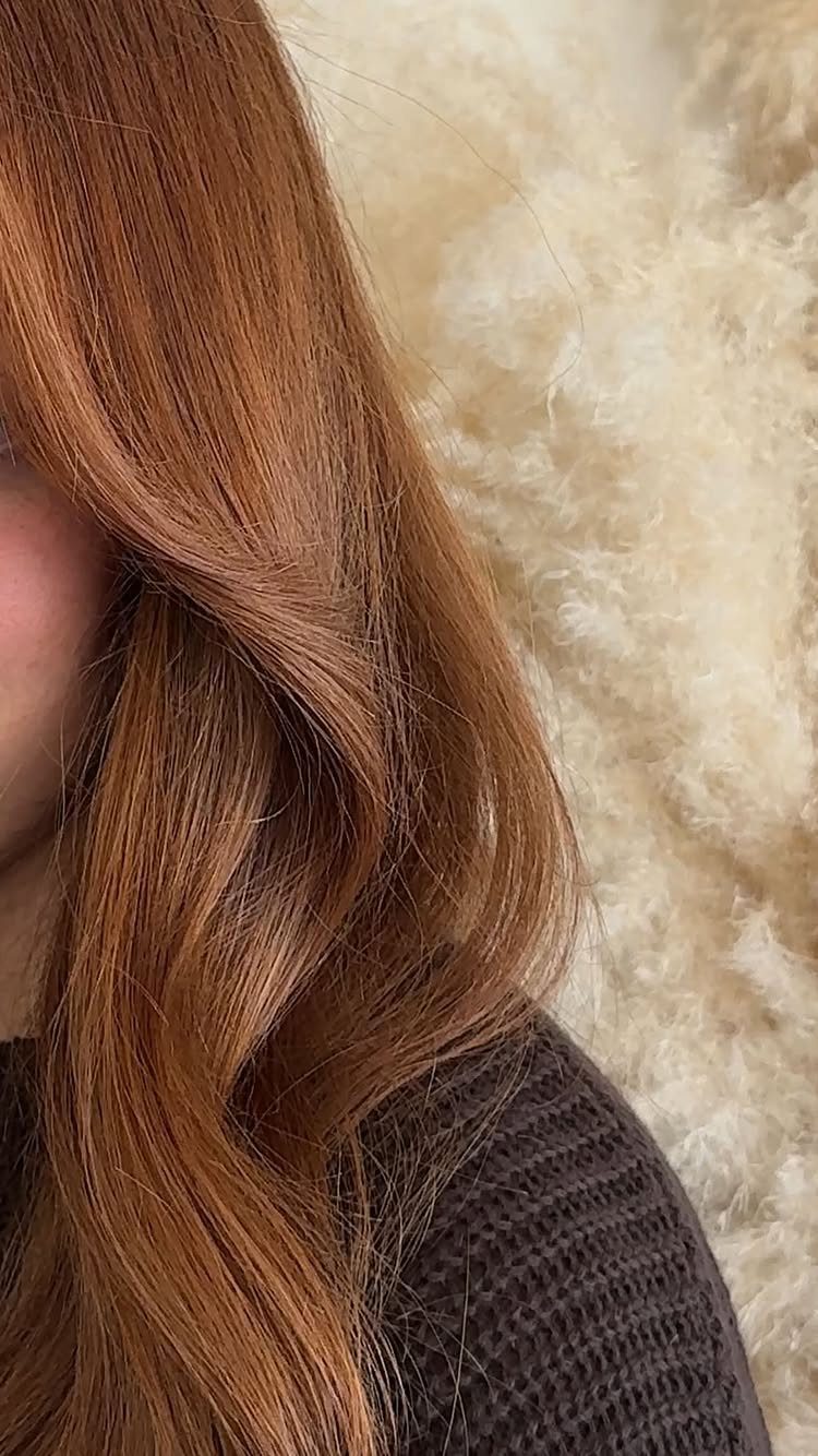 Long copper auburn hair falls in smooth waves over a dark sweater