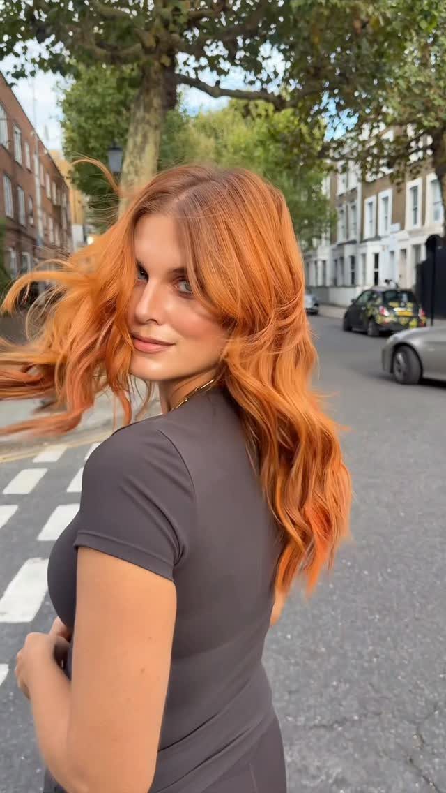 Woman with long, wavy golden copper hair looking back on a city street