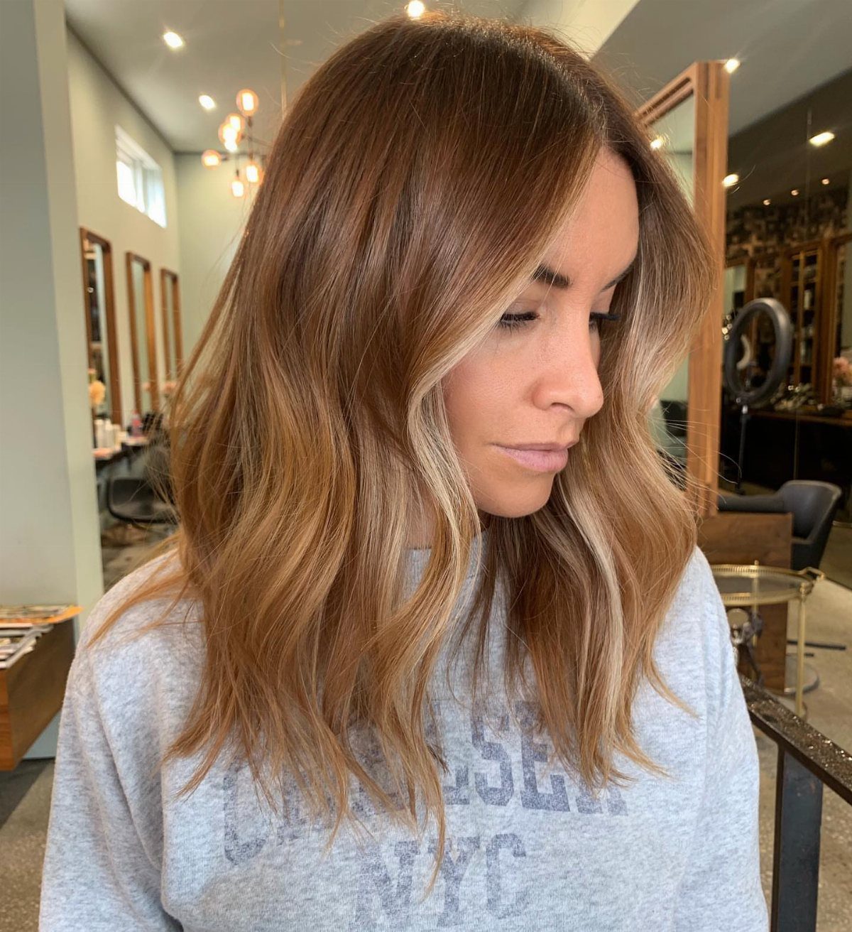 Woman with wavy brown hair and golden copper face-framing highlights in a salon