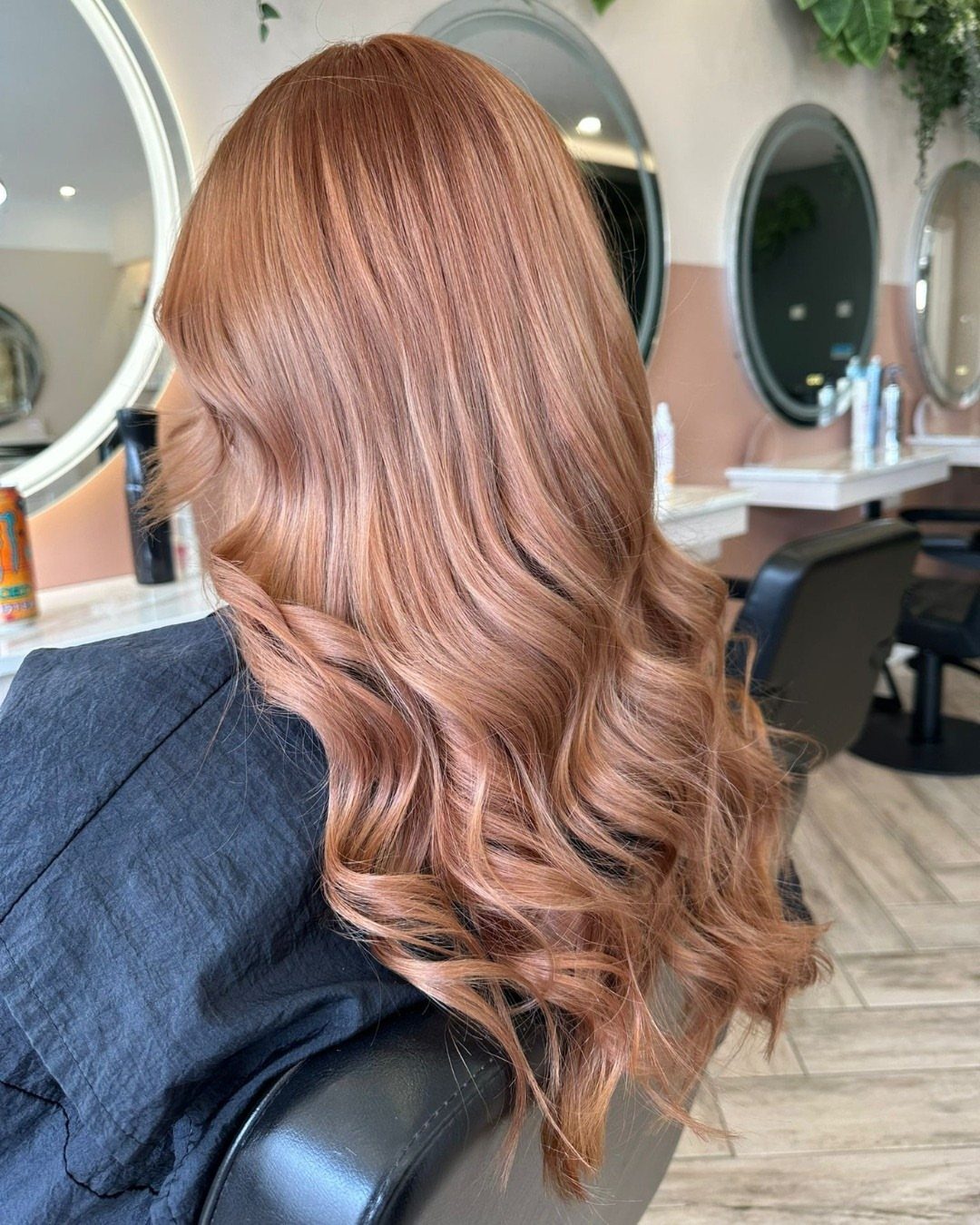 Rose-copper hair styled in long, glossy curls in a salon chair
