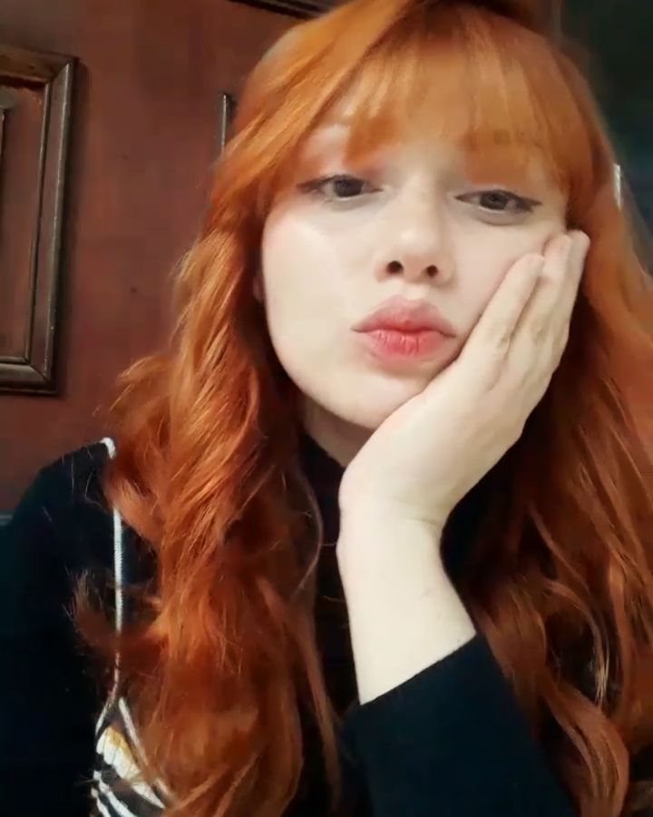 Woman with long, wavy copper-red hair and bangs posing indoors