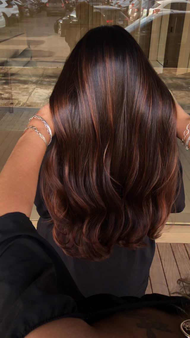 Long dark copper hair falls in glossy, softly curled waves