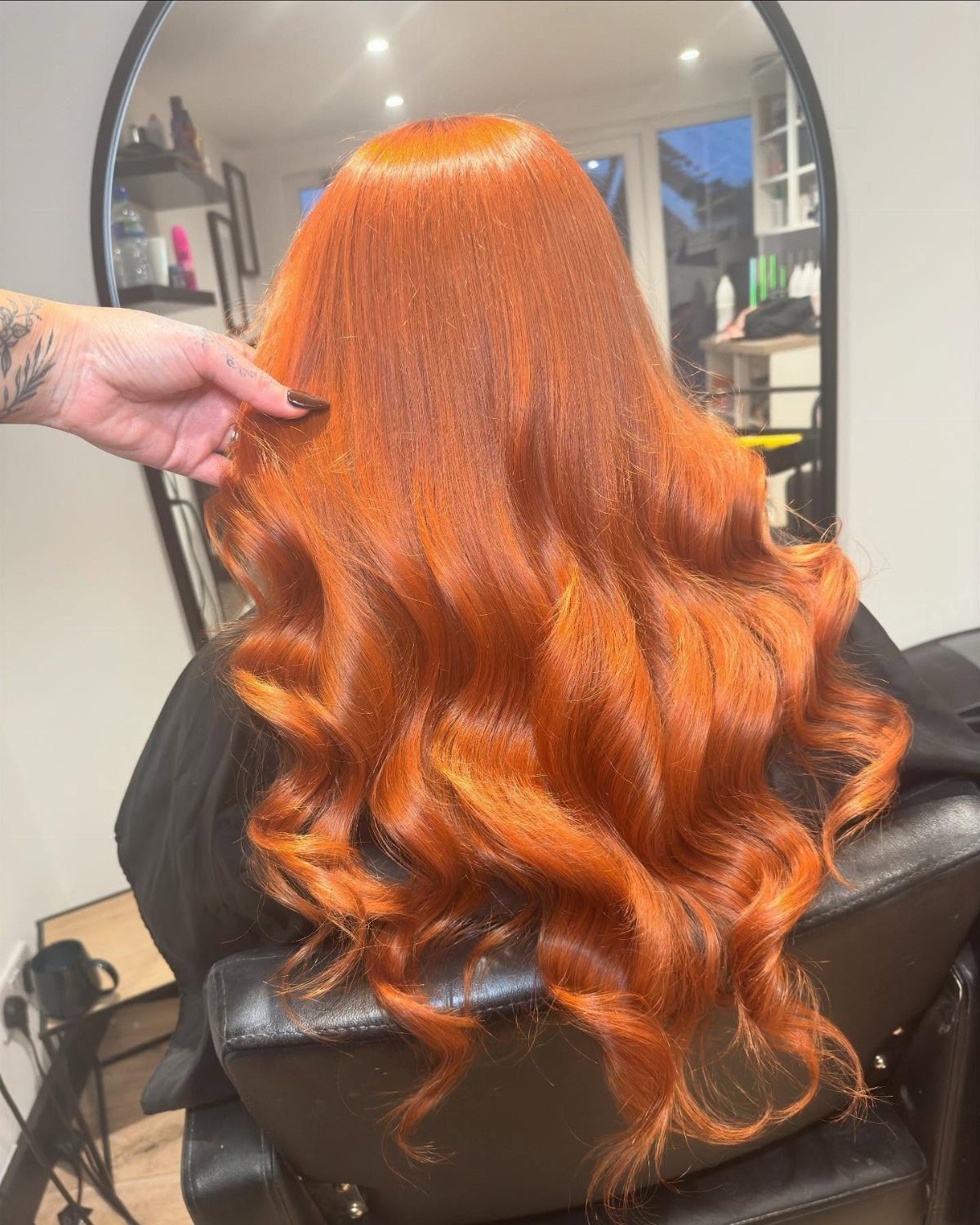 Vivid orange-copper curls cascade down the back of a salon client