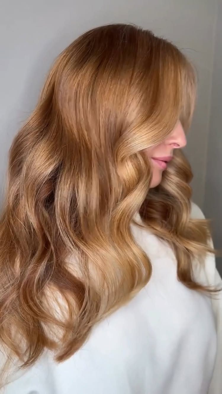 Woman with long honey-copper curls and darker roots against a gray background