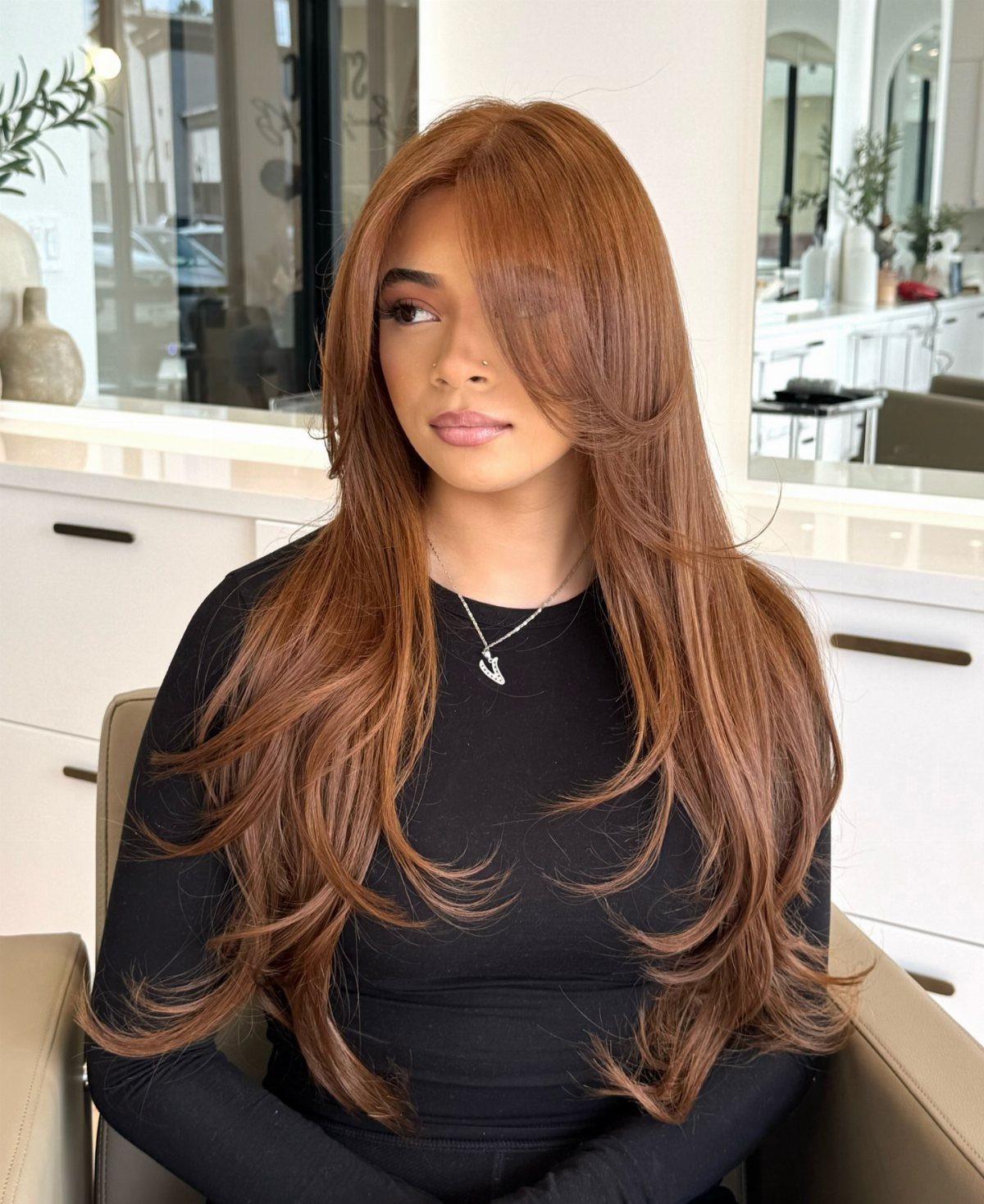 Woman with long, glossy copper-brown hair seated in a bright salon