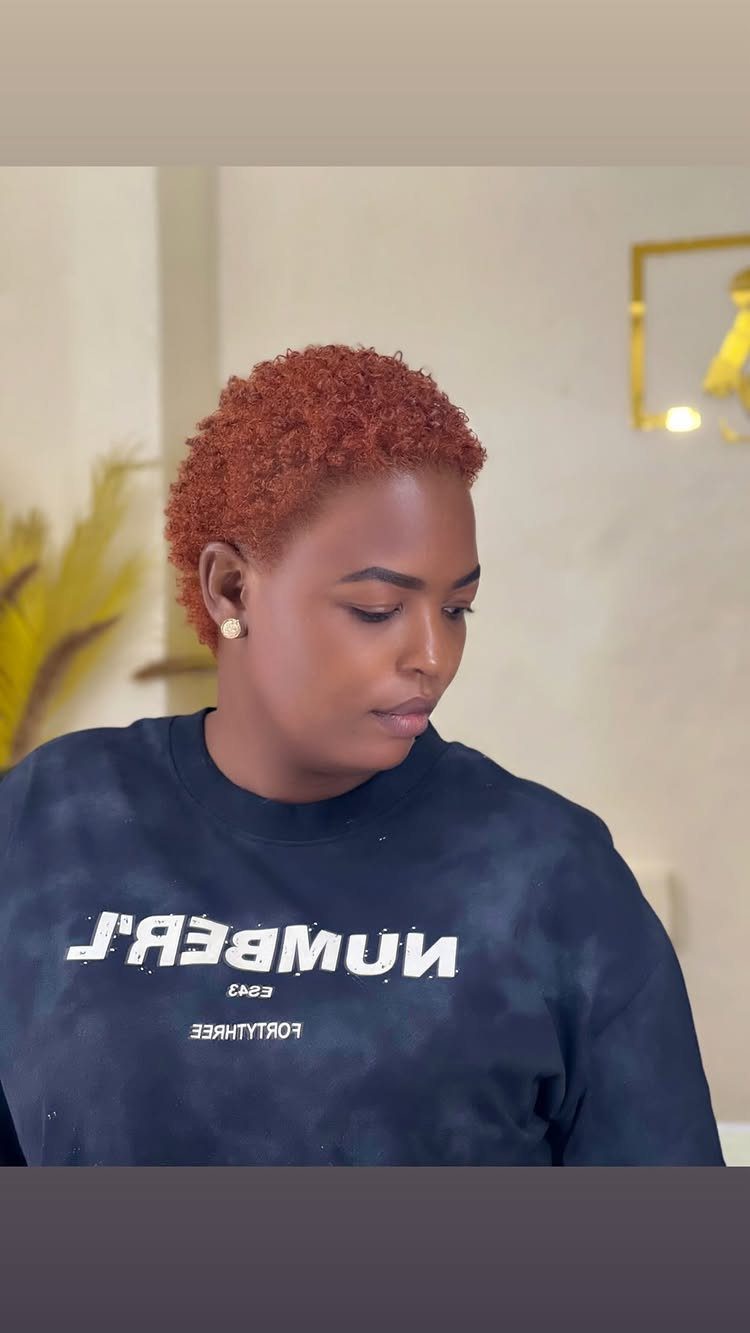 Person with short copper-red curls wearing a navy shirt indoors