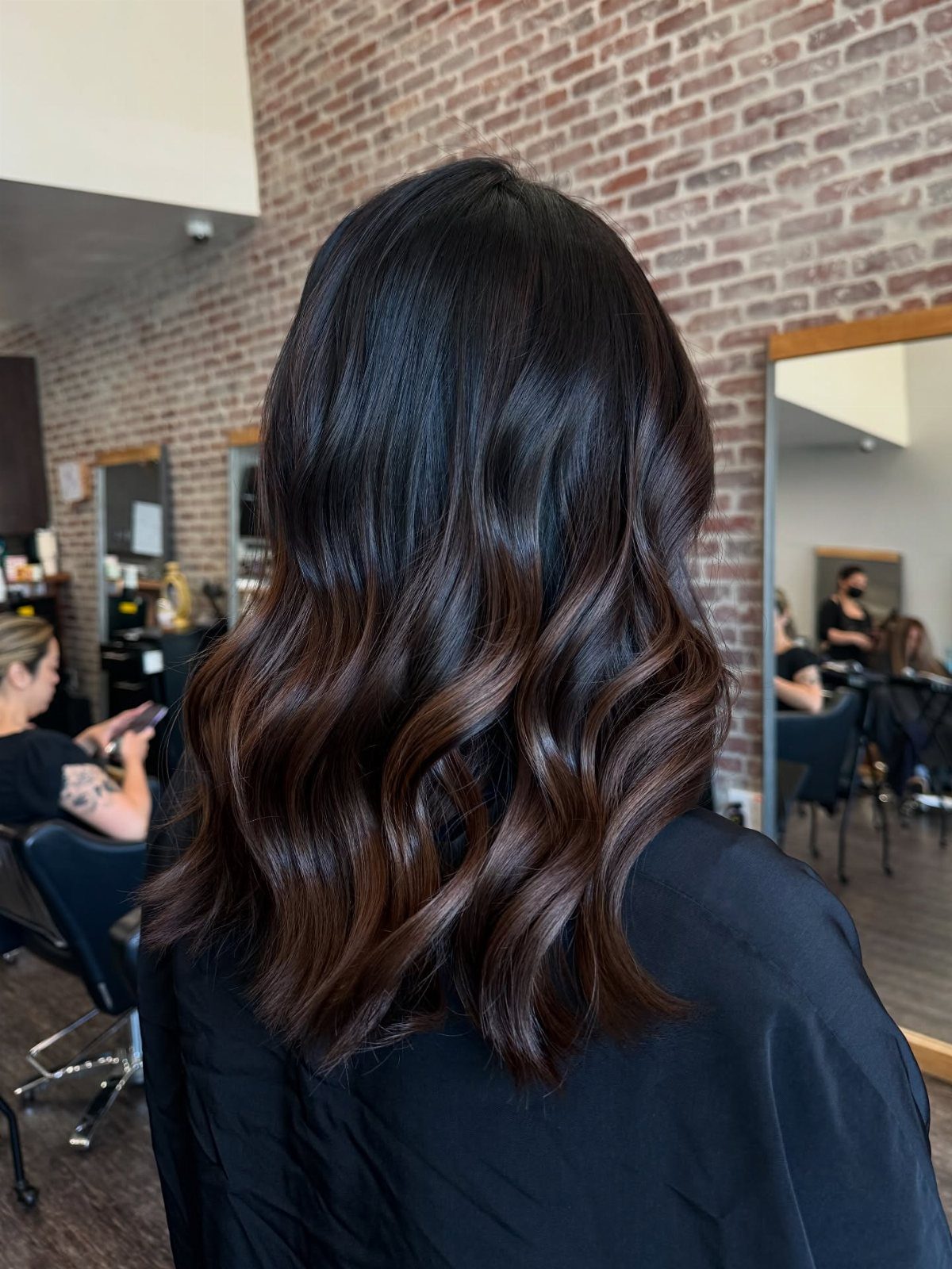 Wavy dark brown hair fades subtly to lighter brown ends in a salon