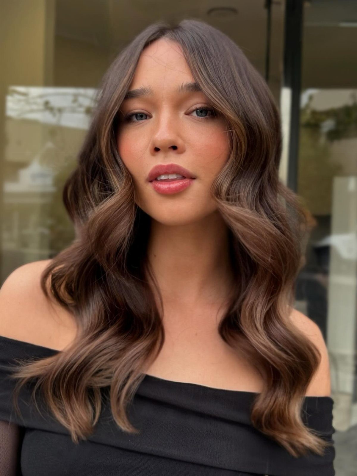 Woman showcasing long wavy butterscotch brown hair with warm lighter highlights