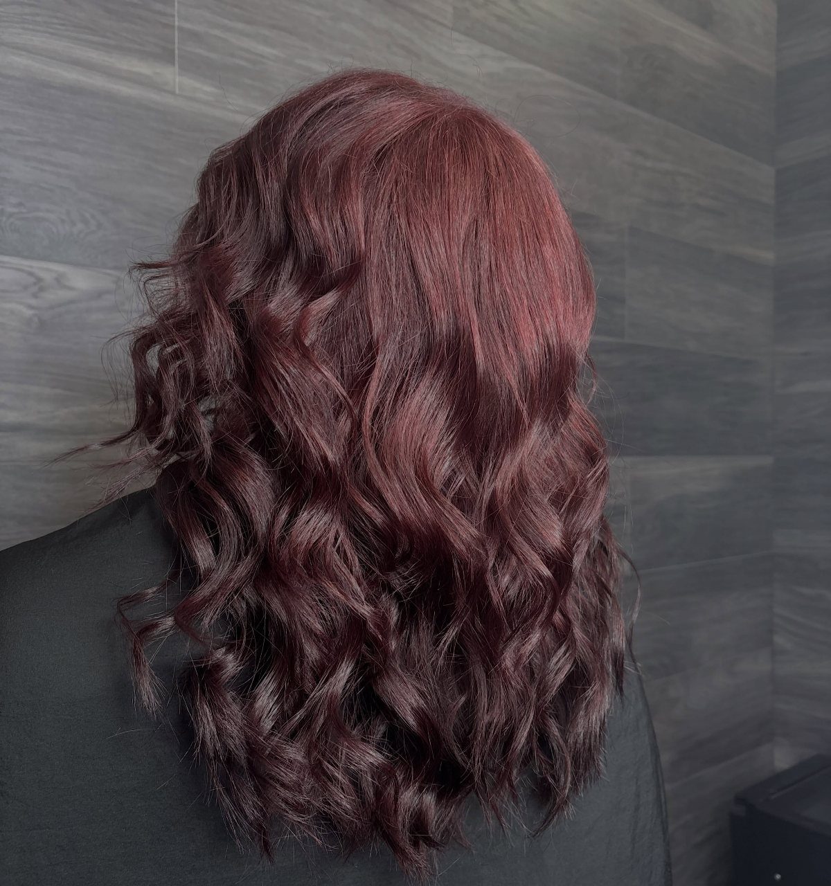 Wavy dark brunette hair shows glossy burgundy and cherry-red accents